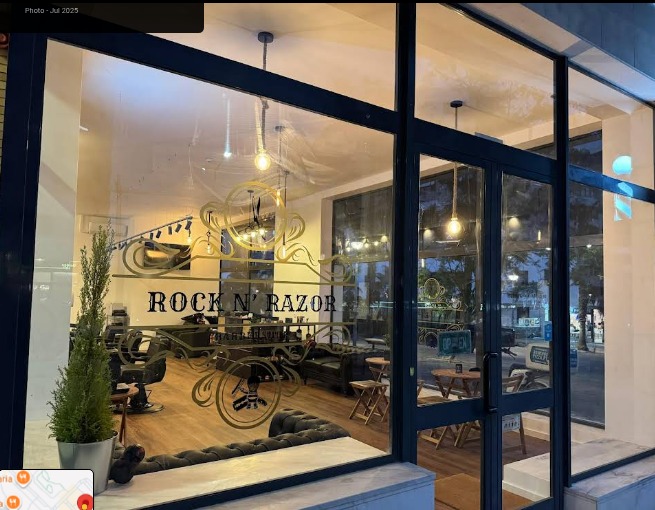 Fachada da Rock n Razor Barbershop com letras no vidro e interior iluminado