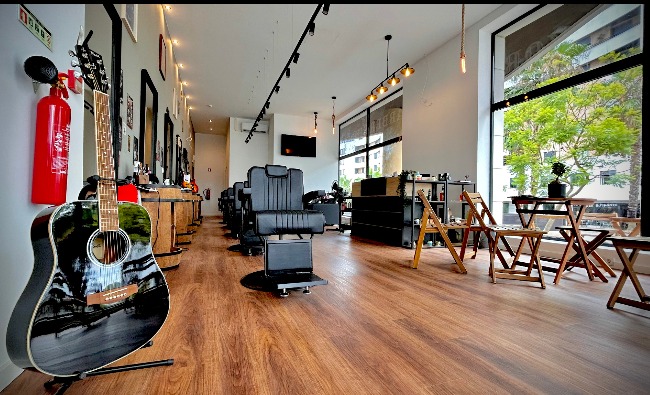 Interior da barbearia com guitarra preta, extintor vermelho e vista para o exterior verde